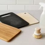 “Skärbrädor i trä, plast och komposit ligger på diskbänk med rengöringsmedel och borste – symboliserar noggrann rengöring och hygien i köket för olika material”